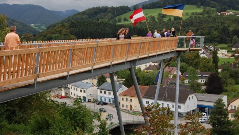 Aussichtsplattform Eröffnung, © Gerhard Hackner Menschen auf einer Holzplattform mit österreichischer und ukrainischer Flagge, im Hintergrund eine ländliche Landschaft.