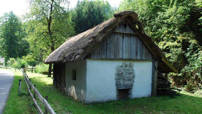 Dörrhaus, © Schager Peter Ein traditionelles Dörrhaus mit Strohdach in einer ländlichen Umgebung, umgeben von Bäumen und Wiese.
