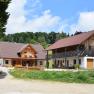 Alm Eibeck, © Groiss Zwei traditionelle Holzhäuser auf einer Alm mit grünem Hügel im Hintergrund.