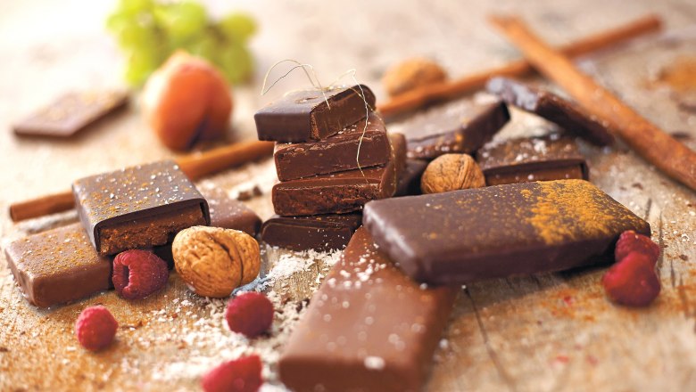 STYX Schokolade, © Styx Naturkosmetic GmbH Verschiedene Schokoladenstücke mit Nüssen und Himbeeren auf einem Tisch.