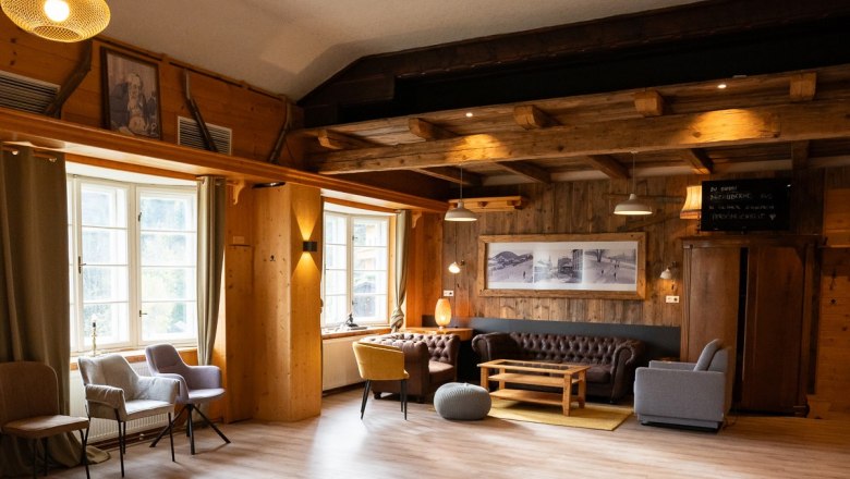 Saal im Kräuterhäusl Puchenstuben, © Kräuterhäusl Puchenstuben Innenansicht eines gemütlichen Raumes mit Holzboden, Ledersofa und mehreren Stühlen. Hängelampen beleuchten den Raum.