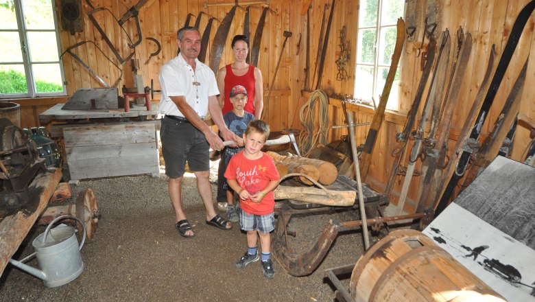 Familie in traditioneller Holzhütte mit alten landwirtschaftlichen Geräten.