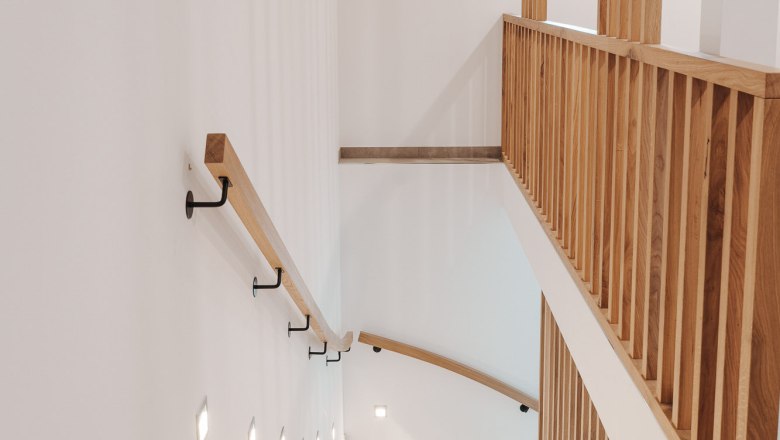 Moderne Treppe mit Holzgel&auml;nder und Wandbeleuchtung in einem hellen Innenraum.