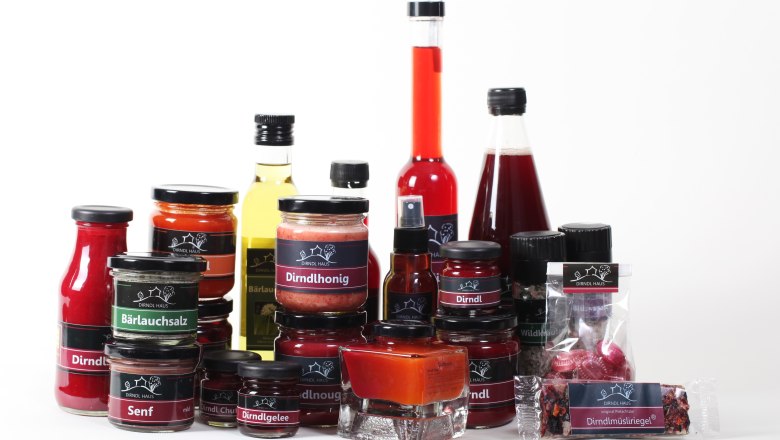 Verschiedene Produkte des Dirndl Haus, darunter Honig, Gelee, Senf und Öl, auf weißem Hintergrund.
