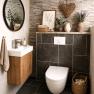 Modernes Badezimmer mit Steinwand, rundem Spiegel, Waschbecken und Dekorationen.