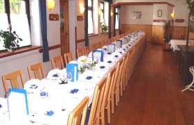 Ein langer, festlich gedeckter Tisch in einem Saal mit Holzboden und Holzdecke.