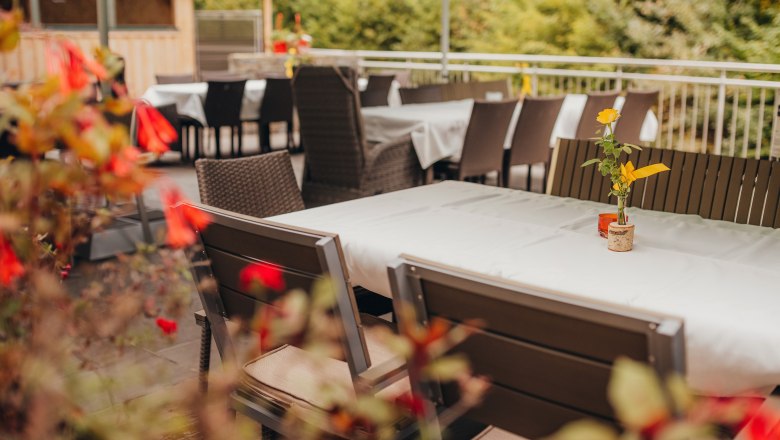 Ein leerer Gastgarten mit gedeckten Tischen und Blumen in Vasen.