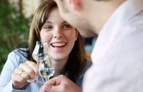 Zwei Personen sto&szlig;en mit Schnapsgl&auml;sern an und l&auml;cheln.