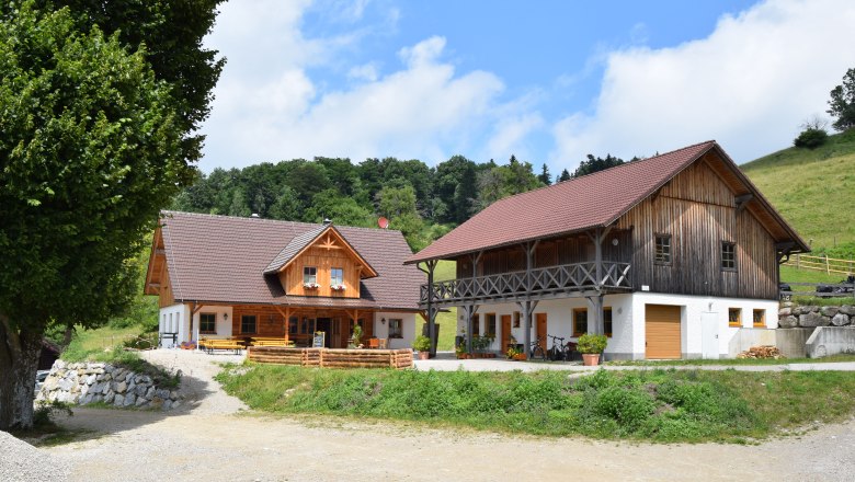 Alm Eibeck, © Groiss Zwei traditionelle Holzhäuser auf einer Alm mit grünem Hügel im Hintergrund.