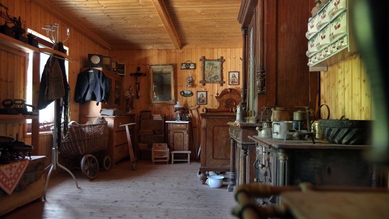 Innenansicht eines traditionellen Bergbauernhauses mit Holzmöbeln und antiken Gegenständen.