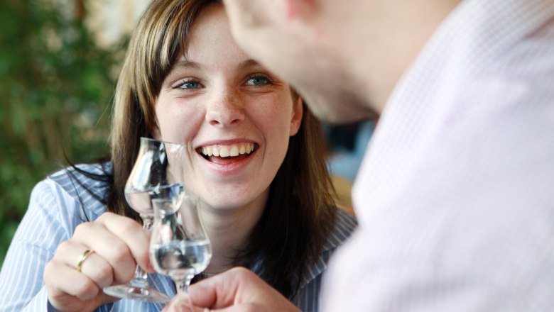 Zwei Personen stoßen mit Schnapsgläsern an und lächeln.
