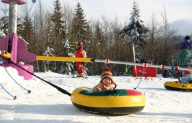 Kinder im Schneepark mit Tubingreifen und Skiausrüstung.