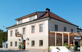 Ein traditionelles Gasthaus mit rosa Fassade und rotem Dach, dekoriert mit Pflanzen und einem Kürbis.
