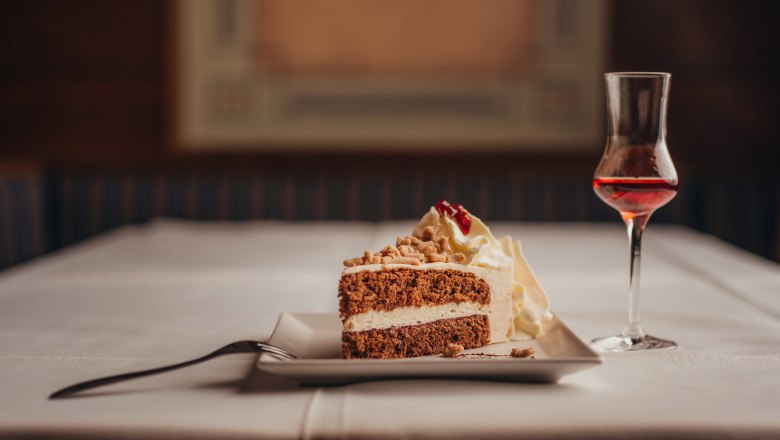 Ein Stück Torte mit Sahne und ein Glas Likör auf einem gedeckten Tisch.