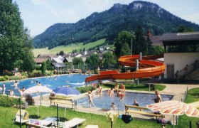 Freibad mit Rutsche und Berglandschaft im Hintergrund.