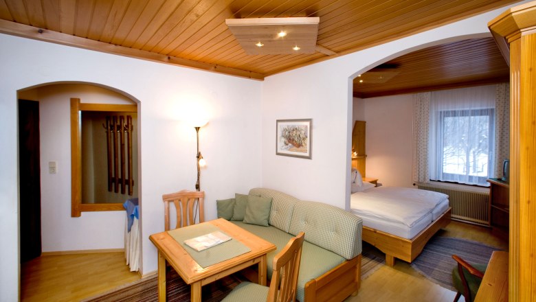 Gemütliches Hotelzimmer mit Holzmöbeln, Esstisch, Sofa und Doppelbett.
