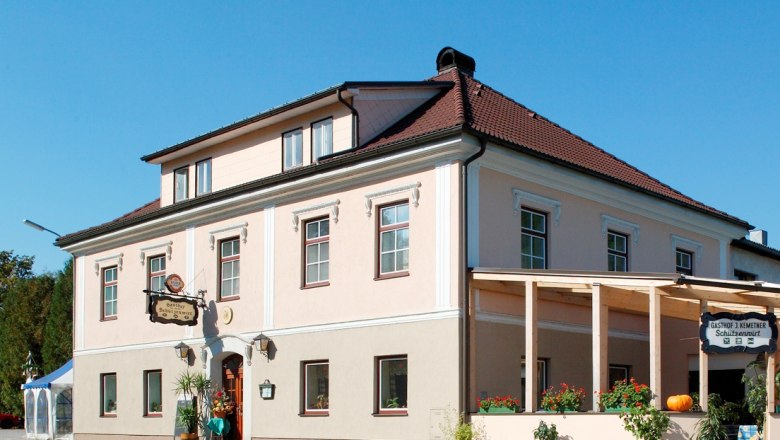 Schützenwirt, © zVg Ein traditionelles Gasthaus mit rosa Fassade und rotem Dach, dekoriert mit Pflanzen und einem Kürbis.