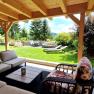 &Uuml;berdachte Terrasse mit Sitzm&ouml;beln und Blick auf einen Garten mit Liegest&uuml;hlen und B&auml;umen.