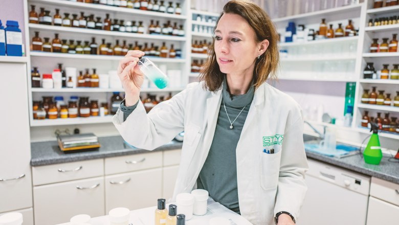 Eine Frau im weißen Laborkittel hält ein Reagenzglas mit blauer Flüssigkeit in einem Labor.