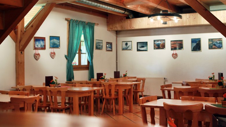 Innenansicht eines rustikalen Gastraums mit Holzmöbeln und Bildern an der Wand.