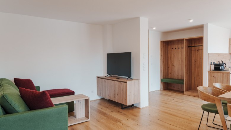 Modern eingerichtetes Wohnzimmer mit gr&uuml;ner Couch, Holzm&ouml;beln und einem Flachbildfernseher.