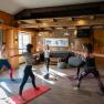 Eine Gruppe Frauen praktiziert Yoga in einem gem&uuml;tlichen Raum mit Holzw&auml;nden und gro&szlig;en Fenstern.