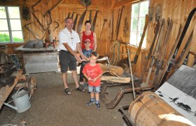 Eine Familie in einem rustikalen Raum mit alten landwirtschaftlichen Werkzeugen und Geräten.