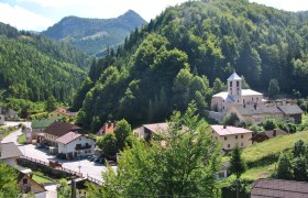 Kleines Dorf in einer gr&uuml;nen Berglandschaft mit Kirche und H&auml;usern.