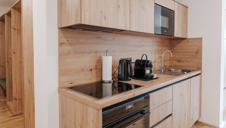 Moderne K&uuml;chenzeile mit Holzverkleidung, Kochfeld, Wasserkocher, Kaffeemaschine und Sp&uuml;le.