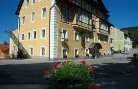 Gelbes Geb&auml;ude mit der Aufschrift 'Hallerhof', Blumen im Vordergrund.