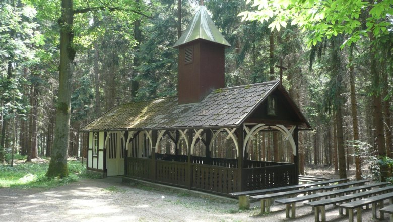Eine kleine Kapelle im Wald mit Holzb&auml;nken im Freien.