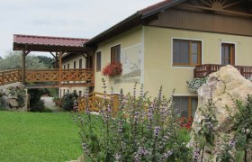 Ein gelbes Gebäude mit Holzbalkon und Blumen, umgeben von grüner Landschaft.