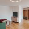 Modern eingerichtetes Wohnzimmer mit gr&uuml;ner Couch, Holzm&ouml;beln und einem Flachbildfernseher.
