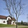 historische Bauernhaus mit roten Dachziegeln und Blumenk&auml;sten vor einem bl&auml;tterlosen Baum auf einer gr&uuml;nen Wiese.