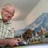 Opa Moser steht vor seiner Modelleisenbahnlandschaft und zeigt eine Lokomotive.